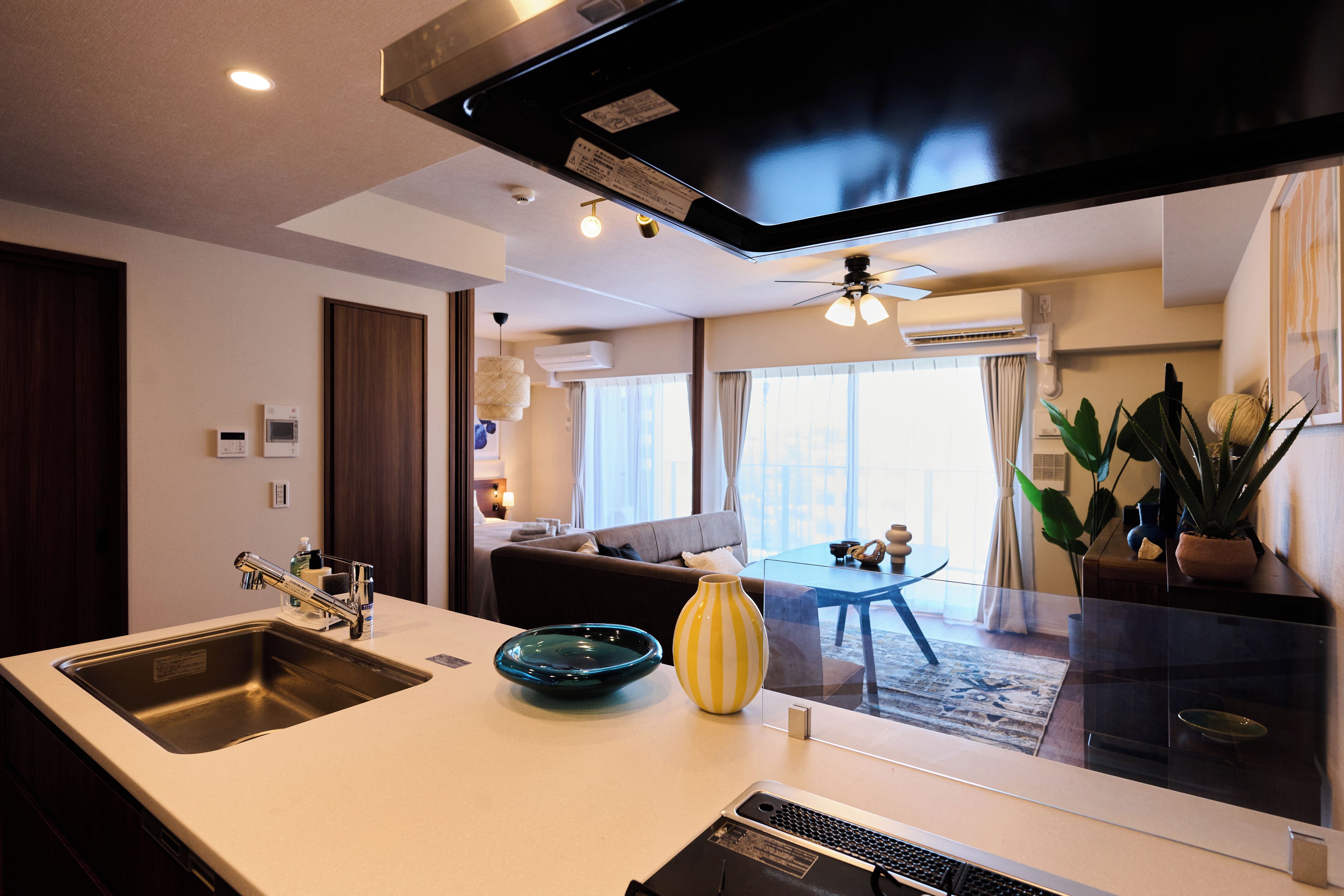 Quarto de hotel moderno com cozinha, área de estar com sofá e mesa de jantar, e vista para o horizonte urbano por grandes janelas.
