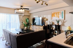 A modern living room with a flat-screen TV, a dining area with a round table, and a kitchen with a sink. - Buranshiera Naha Kainan Puremisuto 905 (Naha)