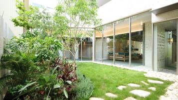 A modern outdoor space with a glass door leading to a seating area, surrounded by lush greenery and a patterned stone pathway.