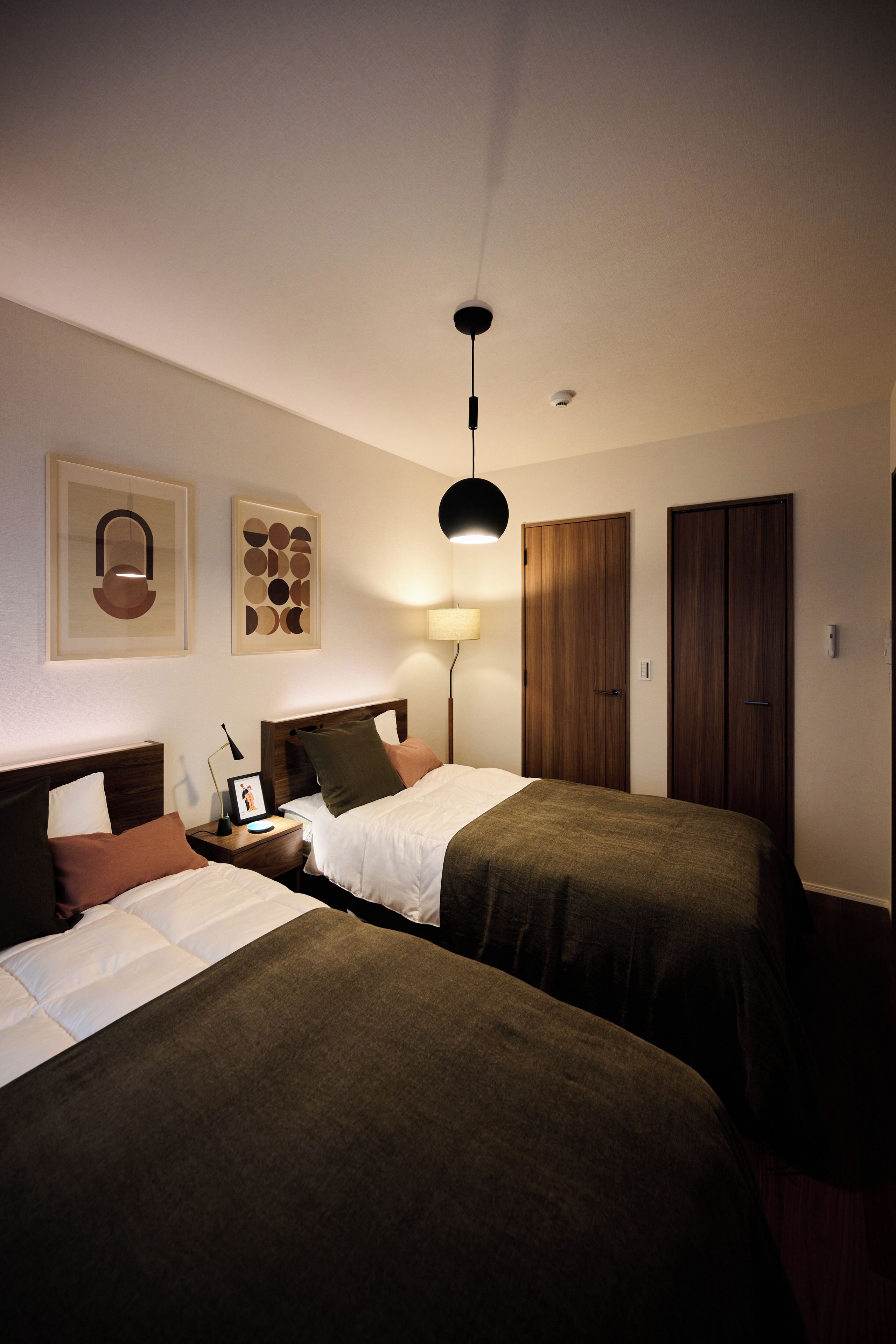 Een hotelkamer met twee bedden, een nachtkastje met een lamp, een lijst met een afbeelding en een kledingkast.