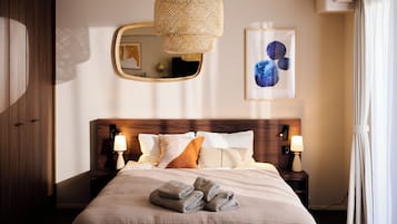 Quarto de hotel com uma cama grande, duas luminárias de cabeceira, um espelho fixado na parede e uma obra de arte emoldurada.