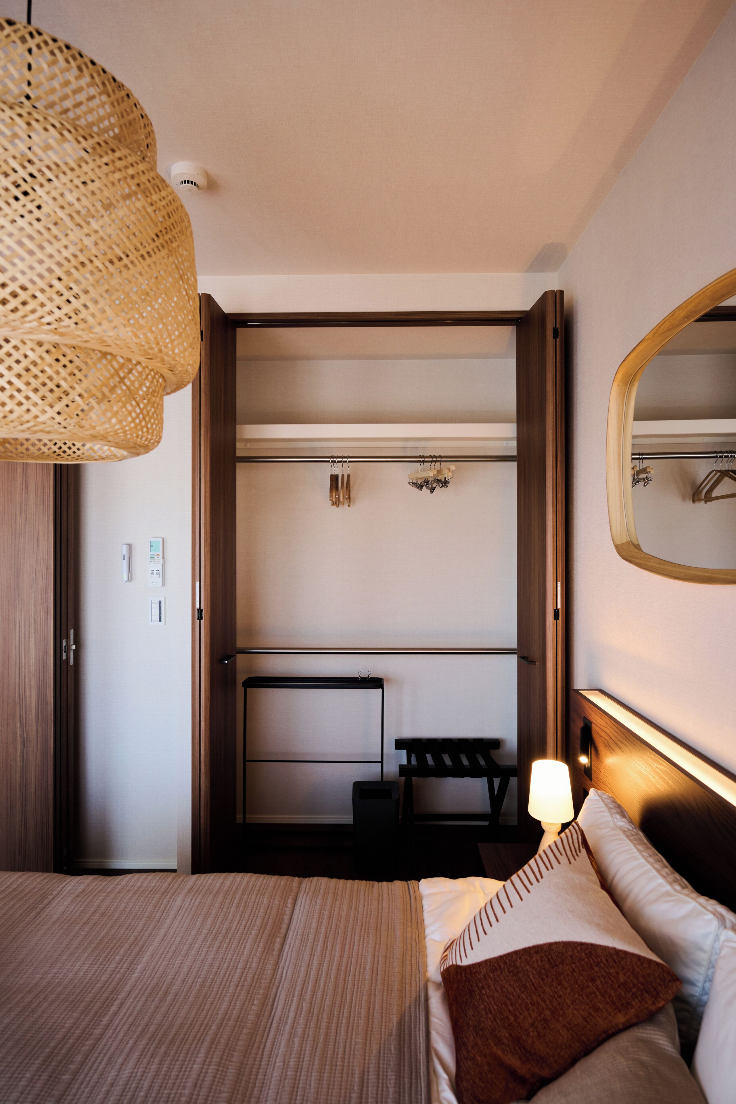 A hotel room with a bed, bedside table, lamp, wardrobe, and a mirror.
