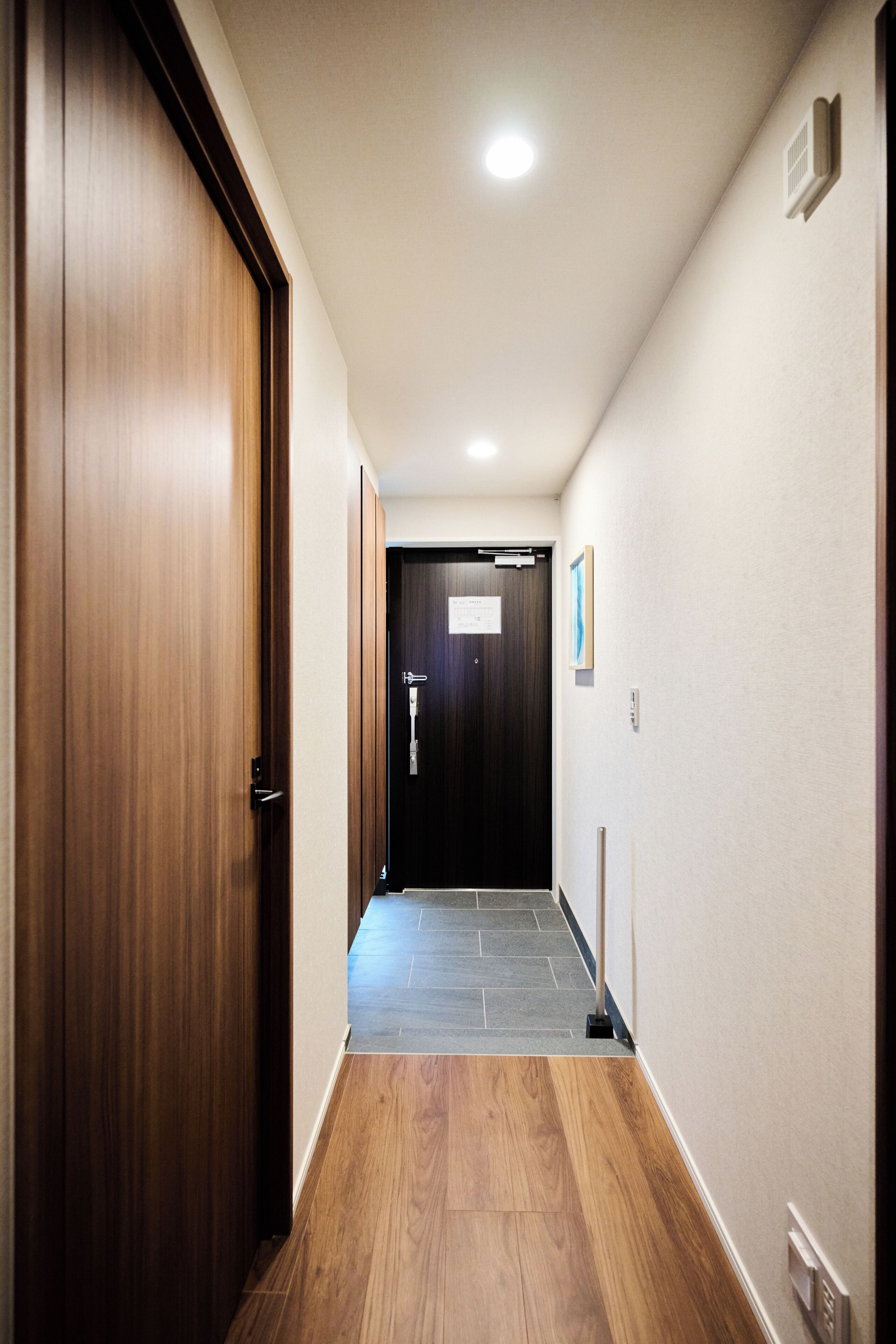 A hallway with wooden flooring, a door with a sign, and a light fixture on the ceiling.