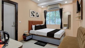 A hotel room with a bed, a desk, a kettle, a phone, and a window with curtains. - Collection O Park Street Road (Kolkata)
