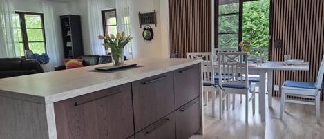 A modern kitchen with a large island, wooden cabinets, and a dining area with white chairs and a table.