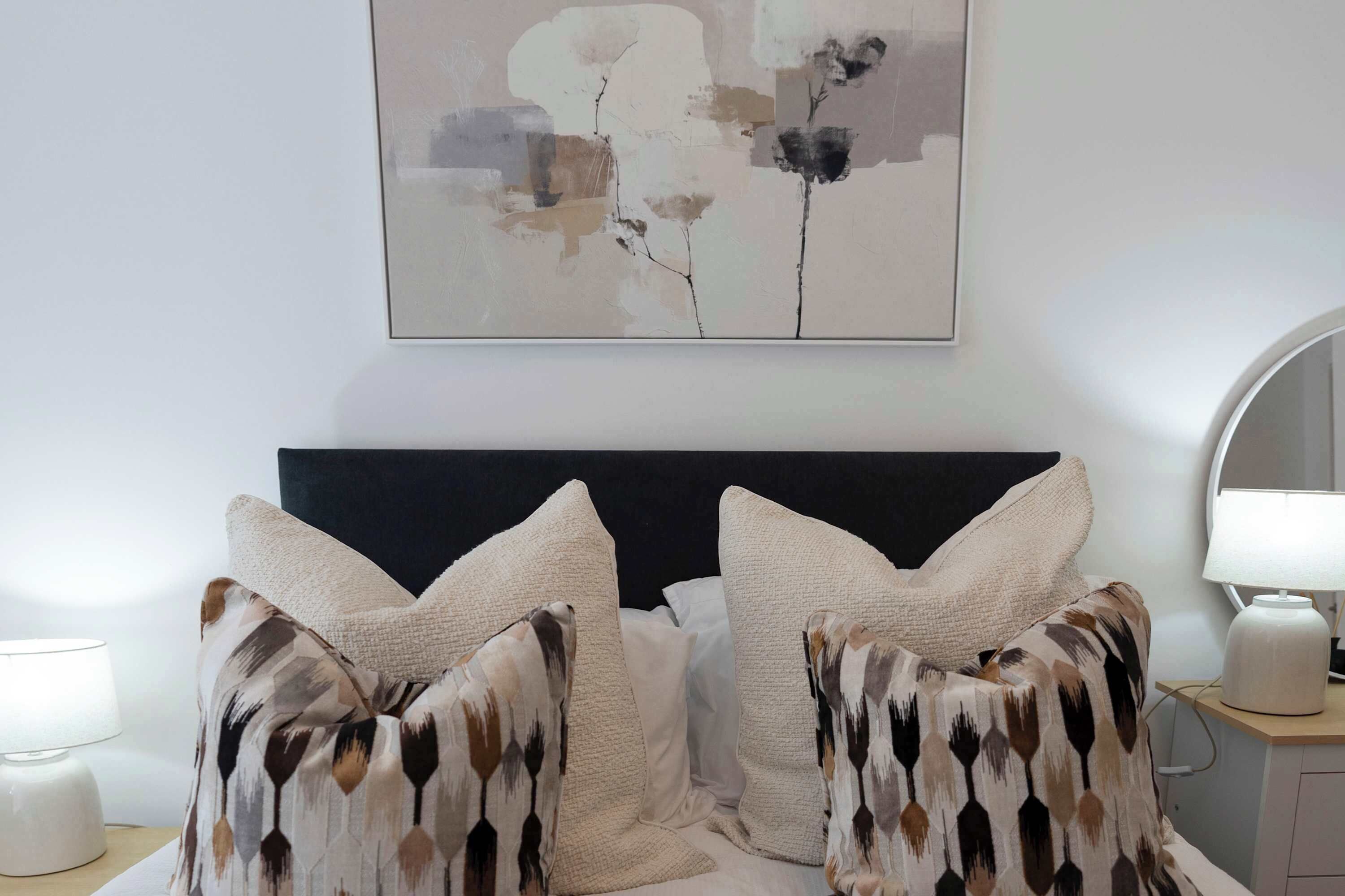 A bedroom with a bed, pillows, a nightstand, a lamp, and a wall-mounted abstract painting.