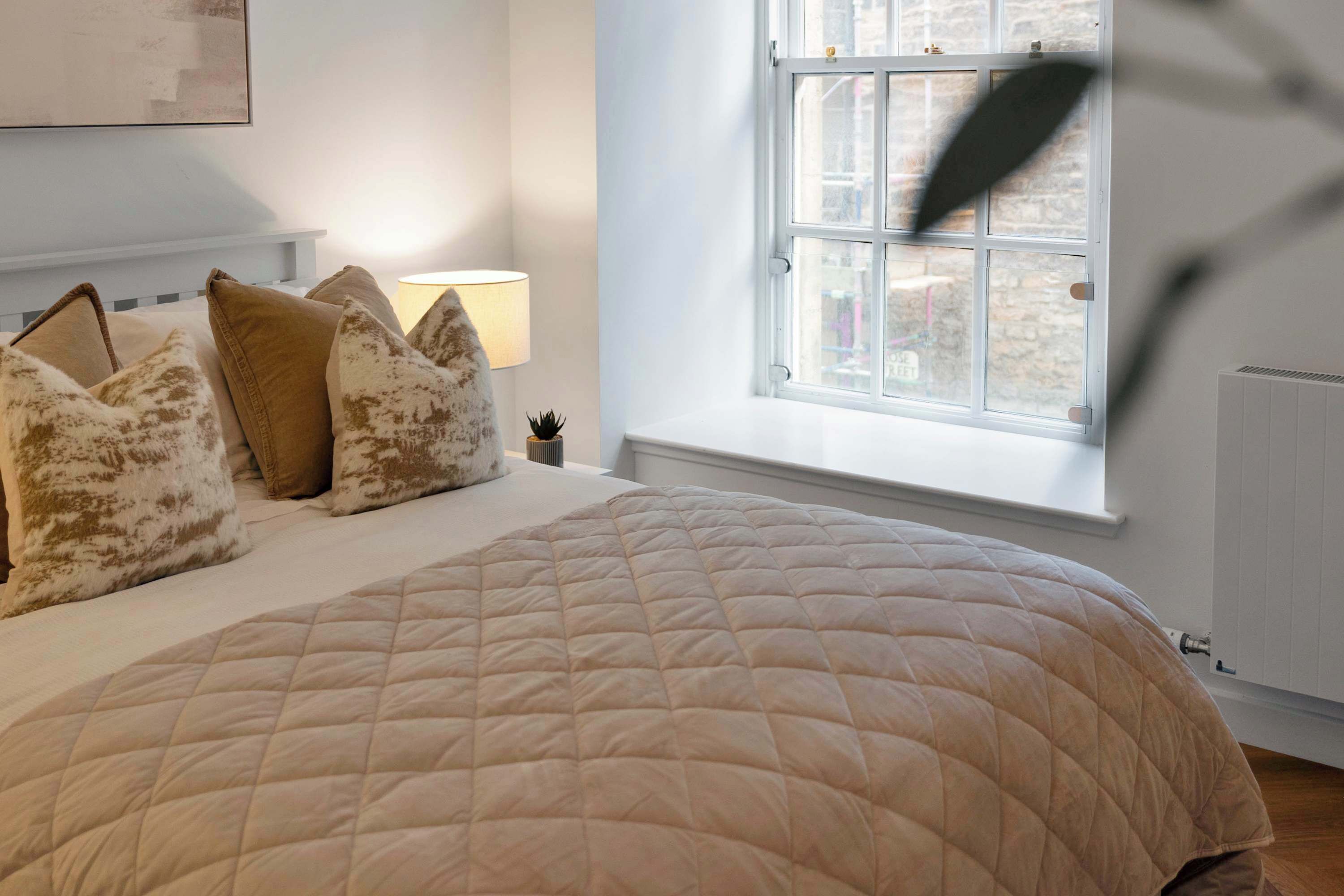 A bedroom with a large bed, a window with a view, and a lamp on the nightstand.