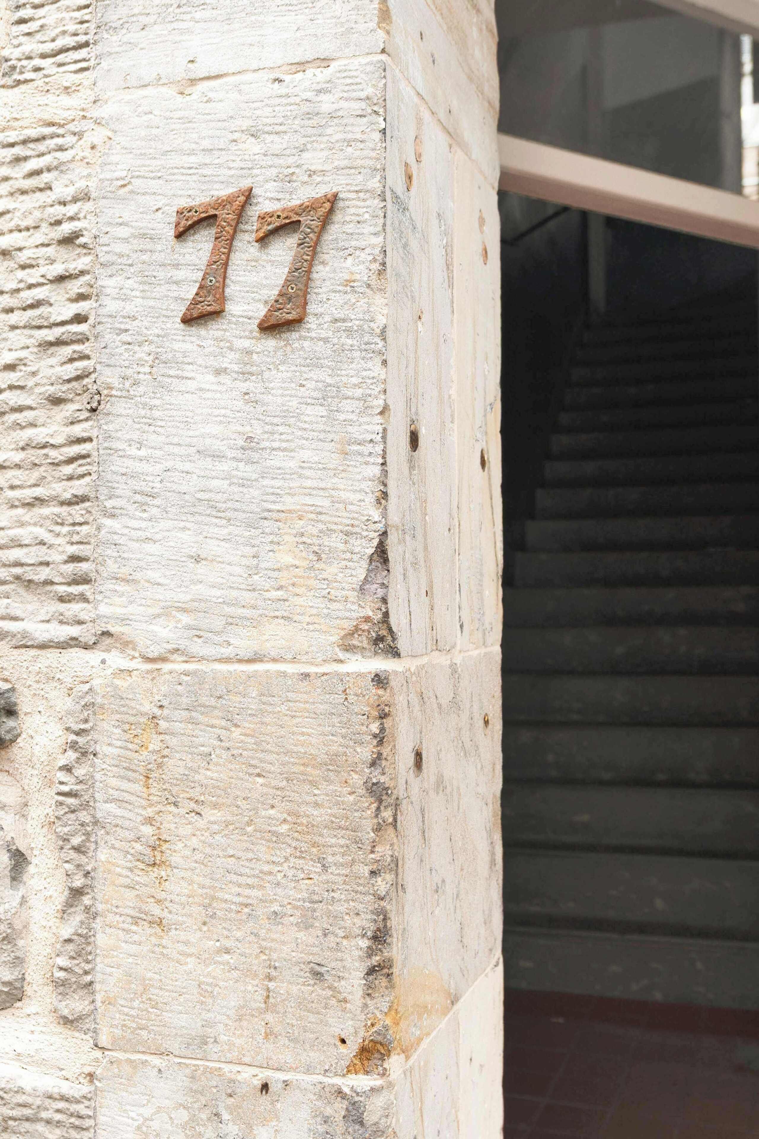 A stone wall with the number '77' mounted on it, indicating a building entrance or location.