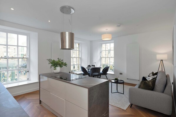 Une cuisine moderne avec un îlot central, un coin repas avec des chaises, un canapé et une lampe.