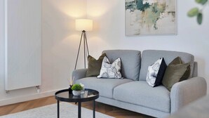 Een moderne woonkamer met een grijze bank, een vloerlamp, een ronde salontafel en een minimalistisch abstract schilderij.