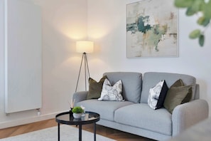 A modern living room with a grey sofa, a floor lamp, a round coffee table, and a minimalist abstract painting. - Modern Apartment in City Centre (Edinburgh)
