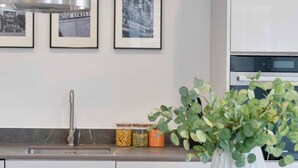 Een moderne keuken met een roestvrijstalen afzuigkap, een wit kastje en een potplant op het aanrecht.