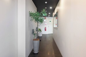 A hallway with a potted plant, a fire extinguisher, and a door with an emergency exit sign.