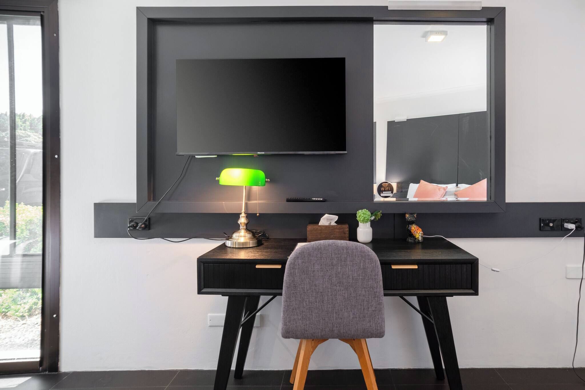 A modern room with a desk, a chair, a flat-screen TV mounted on the wall, and a lamp.