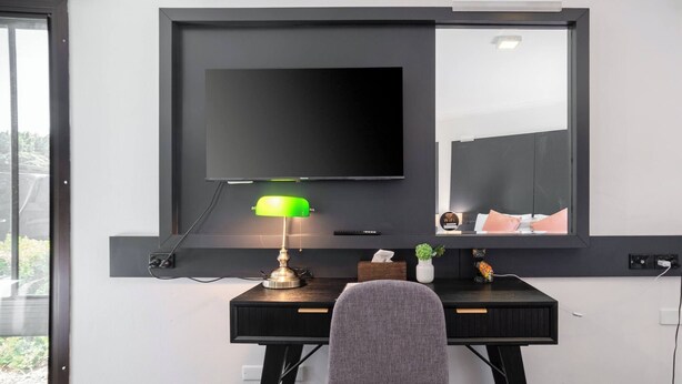 Een moderne kamer met een bureau, een stoel, een wandgemonteerde flatscreen televisie en een lamp.