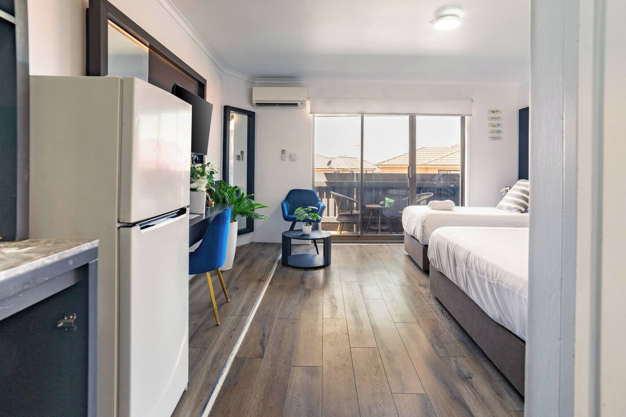 A modern hotel room with a kitchenette, a balcony with a view, and a bed with white bedding.