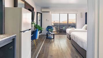 A modern hotel room with a kitchenette, a balcony with a view, and a bed with white bedding.