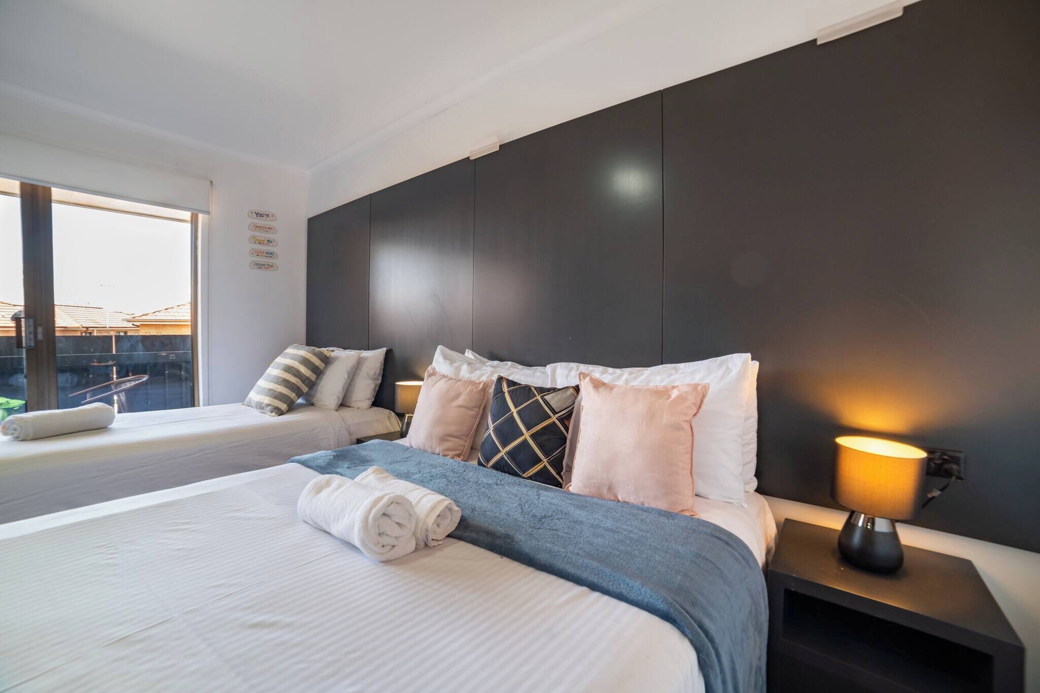 A modern hotel room with a large bed, a smaller bed, a window with a view, and a bedside lamp.
