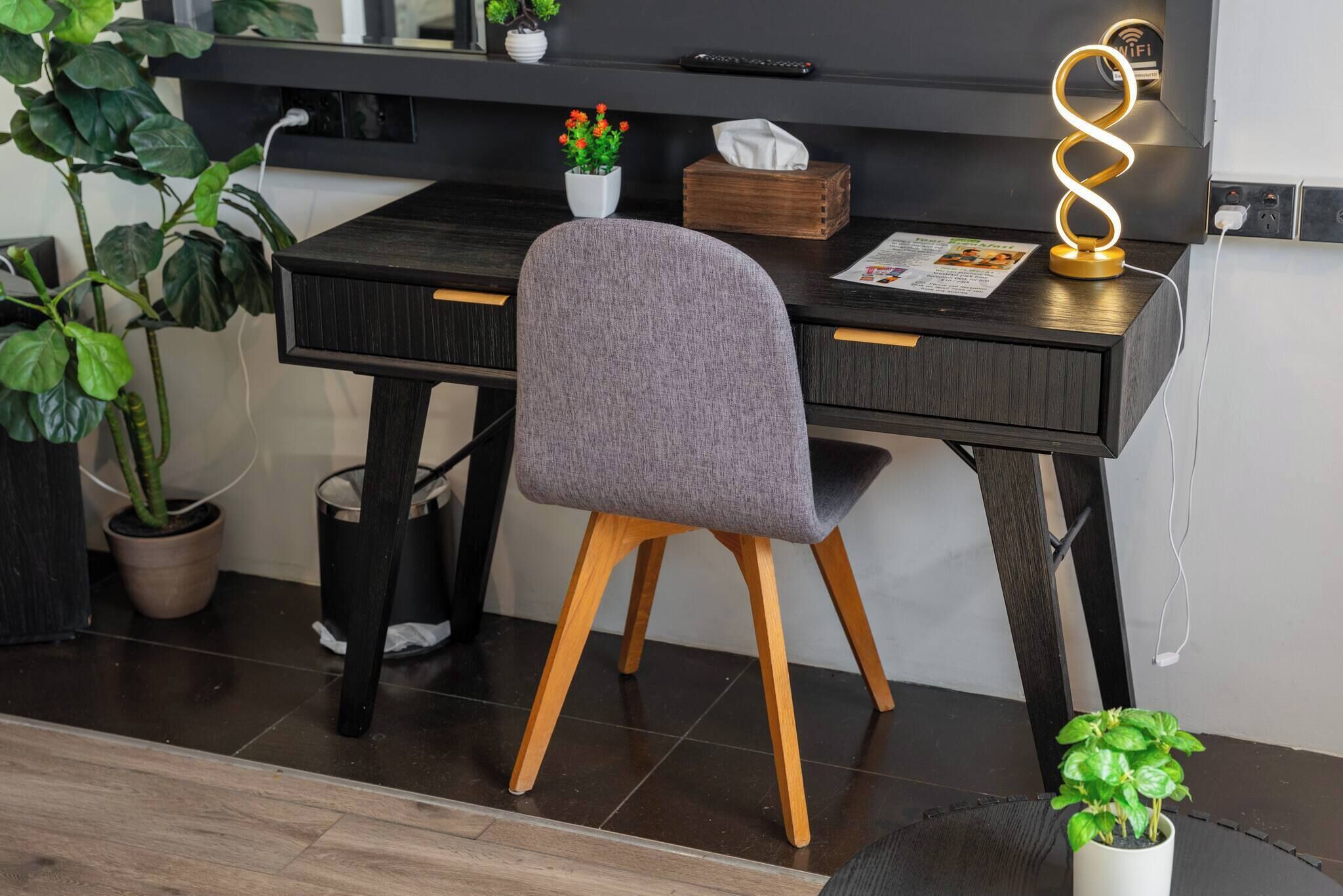 A modern workspace with a desk, chair, potted plants, and a wall-mounted light fixture.