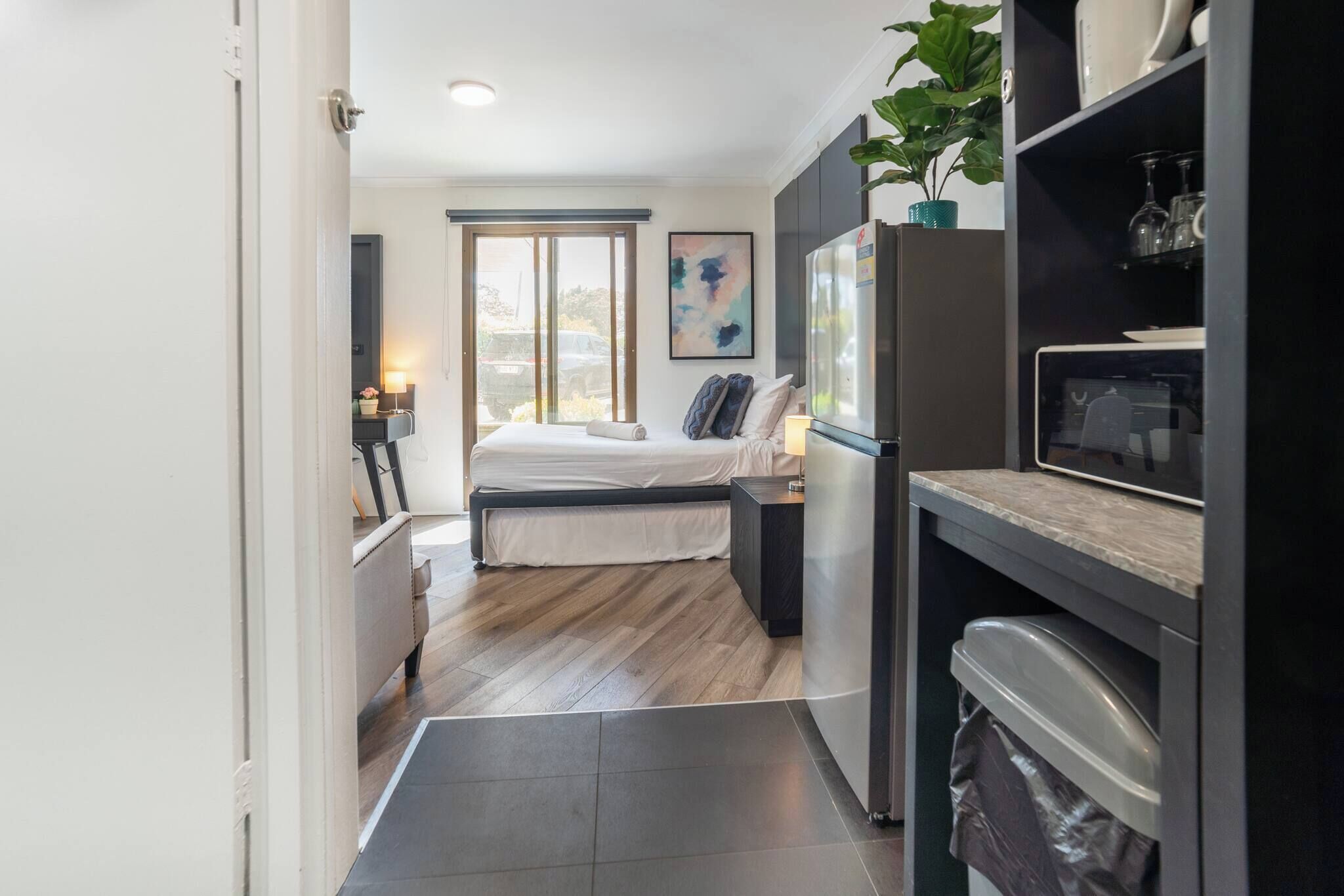 A compact hotel room with a bed, a small desk, a refrigerator, and a microwave.