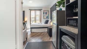 A compact hotel room with a bed, a small desk, a refrigerator, and a microwave.