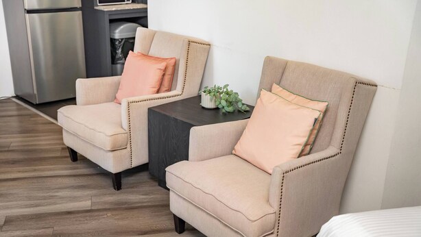 Dos sillones con cojines a juego, una mesita con una planta y una cama en una habitación de hotel con piso de madera.