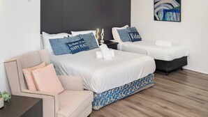 Habitación de hotel con dos camas, un sofá, una mesita de noche y una obra de arte en la pared.