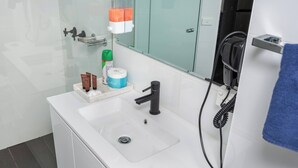 Un baño moderno con lavamanos blanco, espejo, secador de pelo y artículos de aseo.