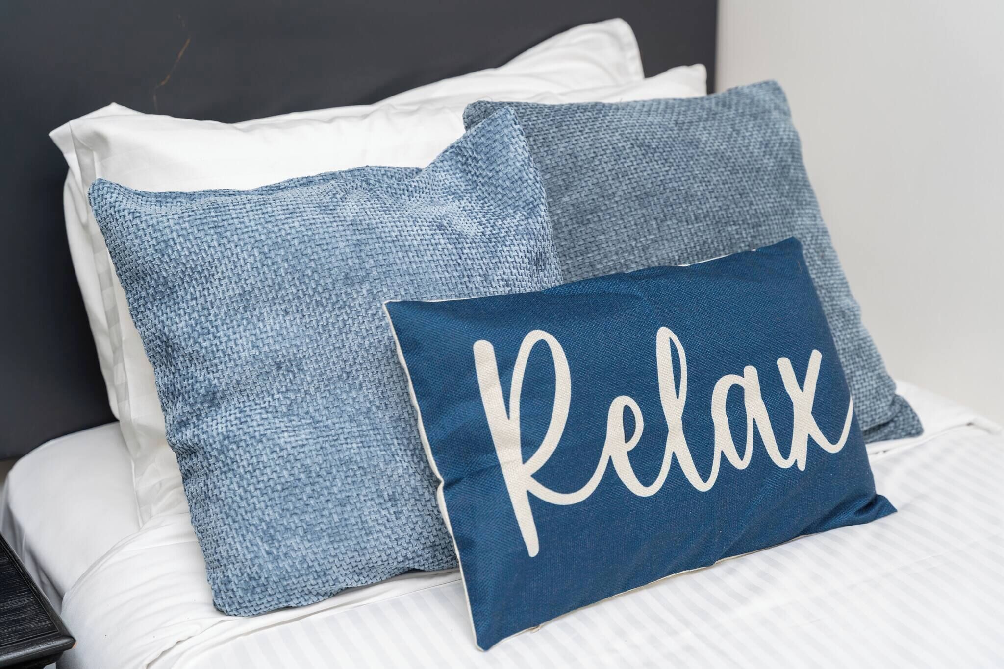 A bed with two pillows, one plain and one with 'Relax' written on it.