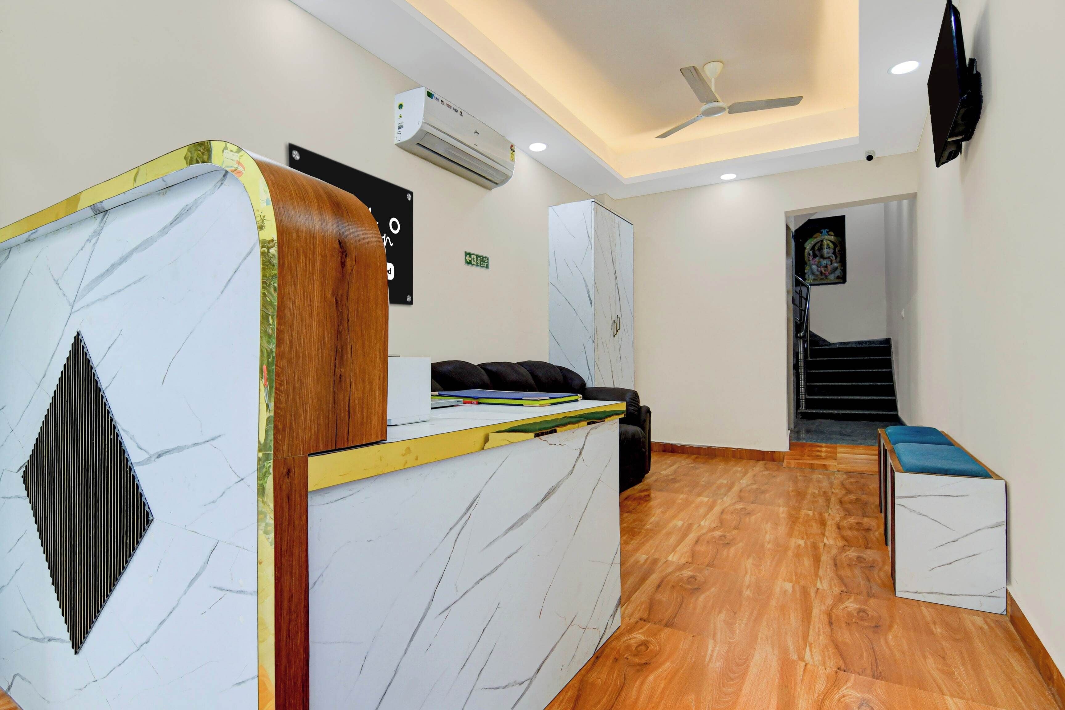 Un espace d’accueil comprenant un comptoir de réception en marbre, un canapé en cuir noir, un escalier et un ventilateur de plafond.
