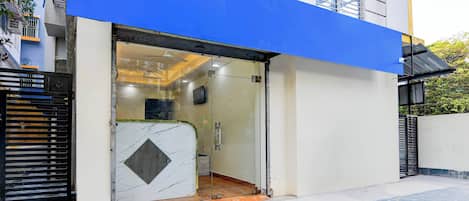A modern building entrance with a glass door, a blue awning, and a tiled ground.