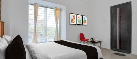 A hotel room with a bed, a window with curtains, a red chair, a small table with a tray, and a door.