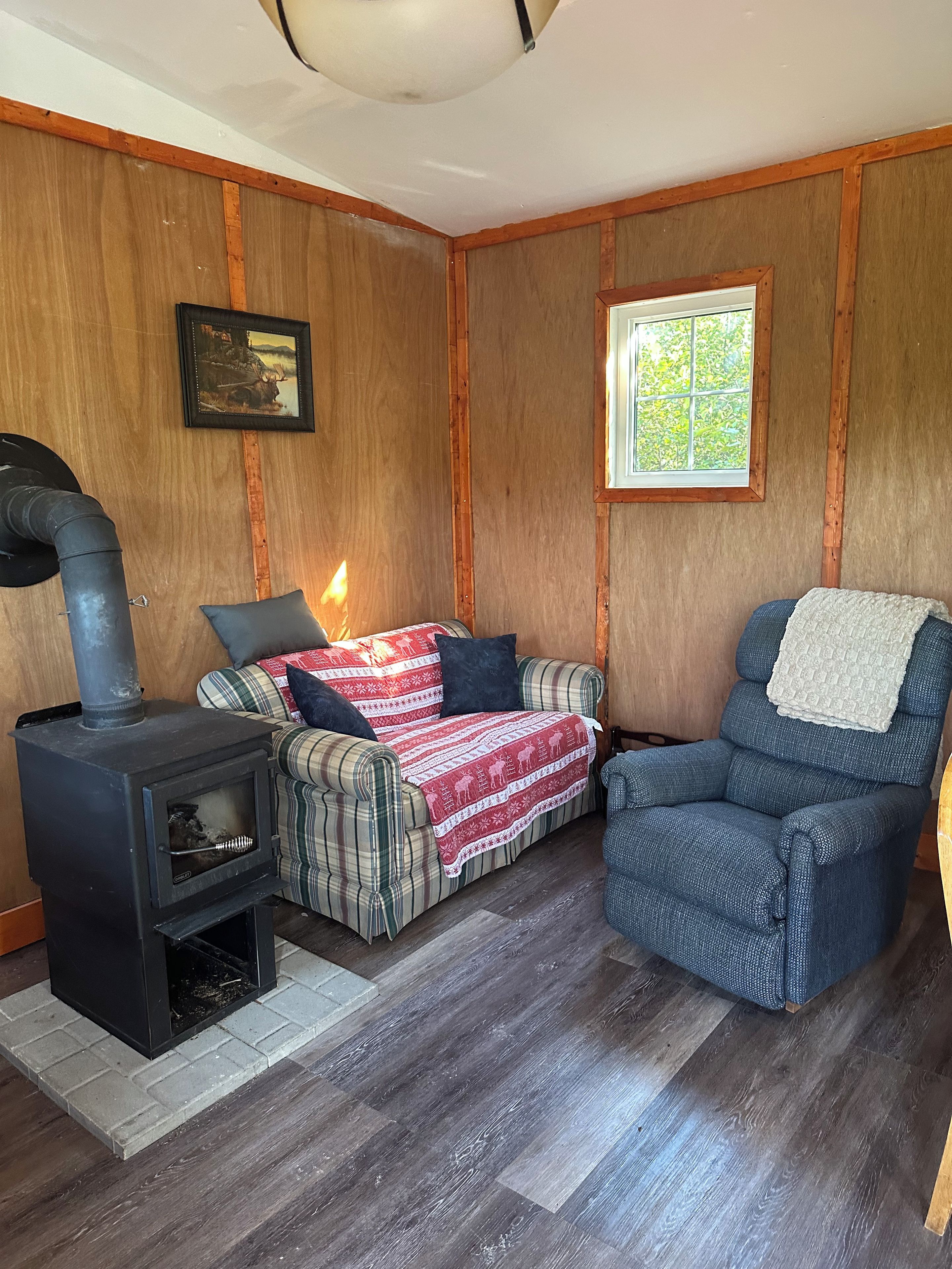 A cozy room with a wood-burning stove, a plaid sofa, and a blue armchair.