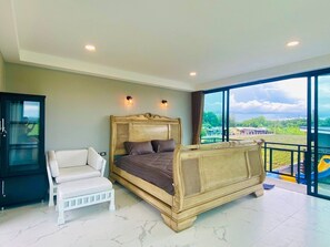 Ein Schlafzimmer mit einem großen Bett, einem weißen Sessel und Blick auf einen Spielplatz durch ein großes Fenster.