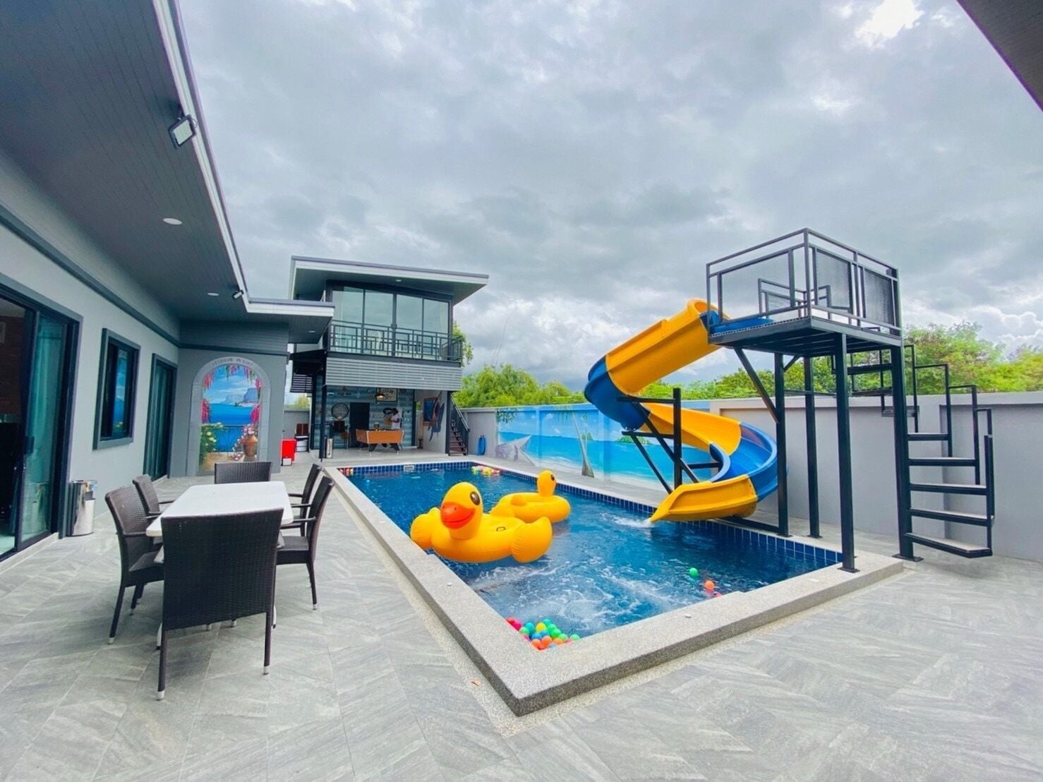 A swimming pool with a slide, outdoor seating, and a two-story building with a balcony.