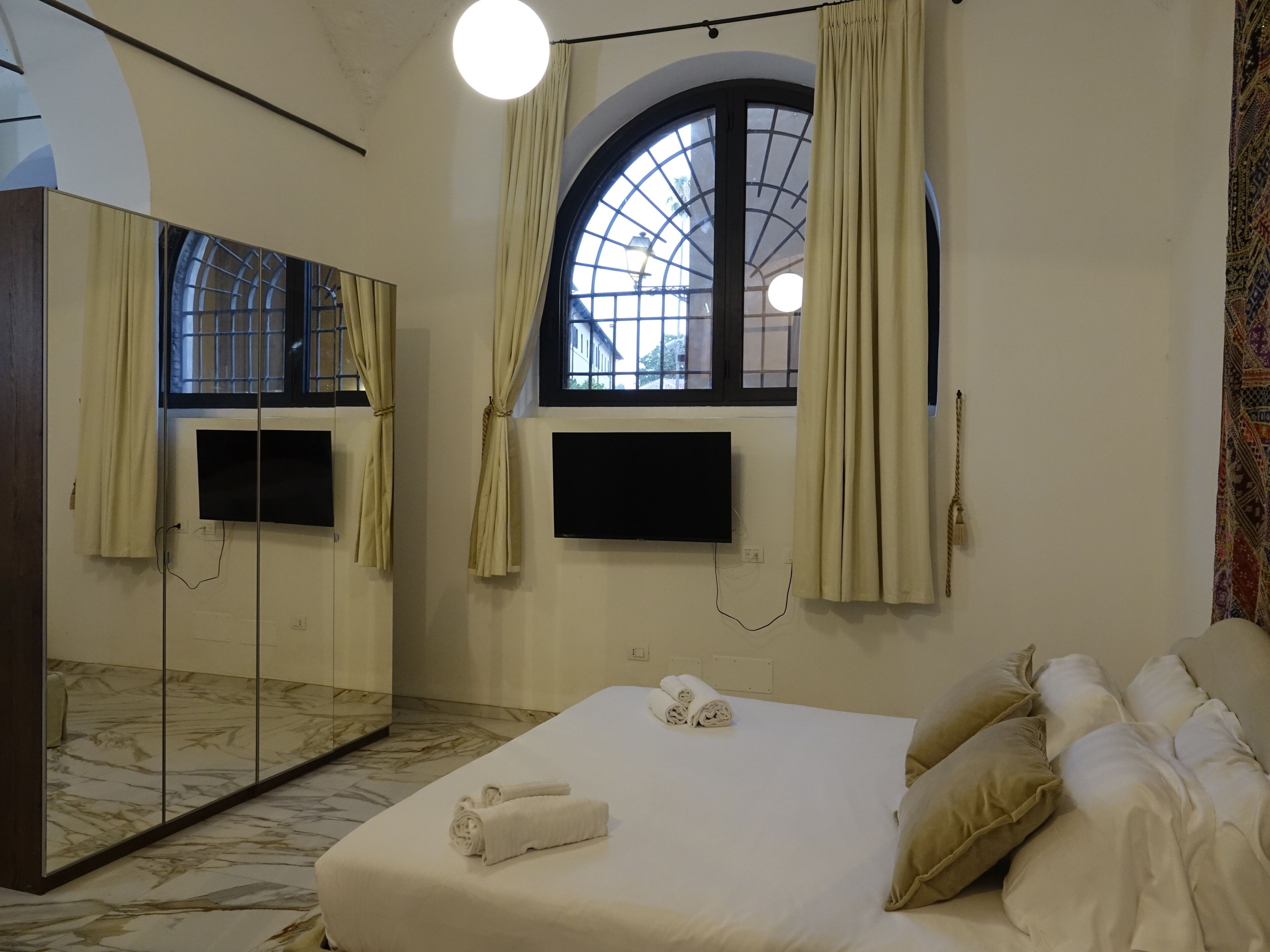 Una habitación de hotel con una cama, un espejo grande, un televisor y una ventana con cortinas.