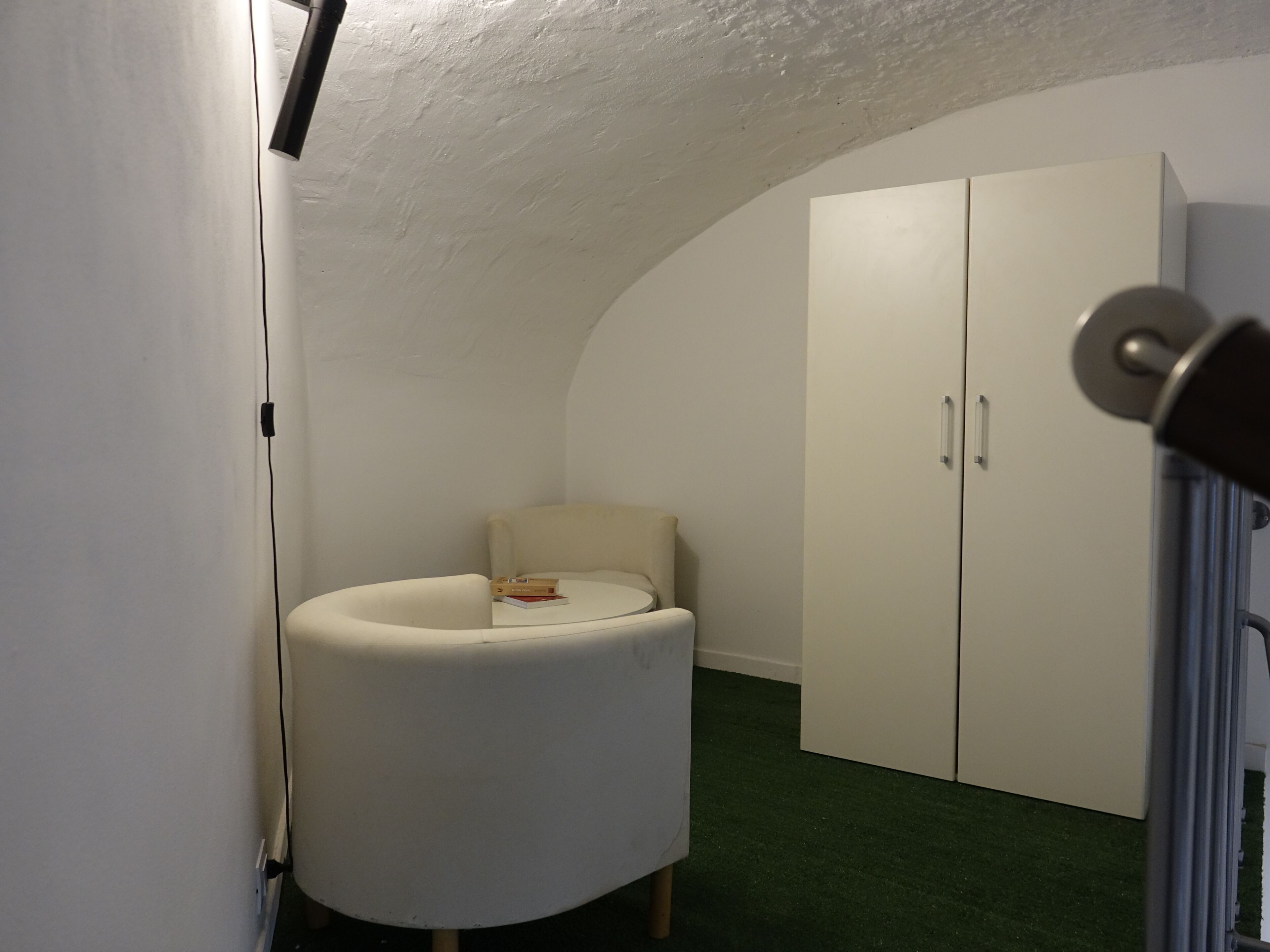 Una habitación con una butaca curvada, un armario y una puerta con picaporte.