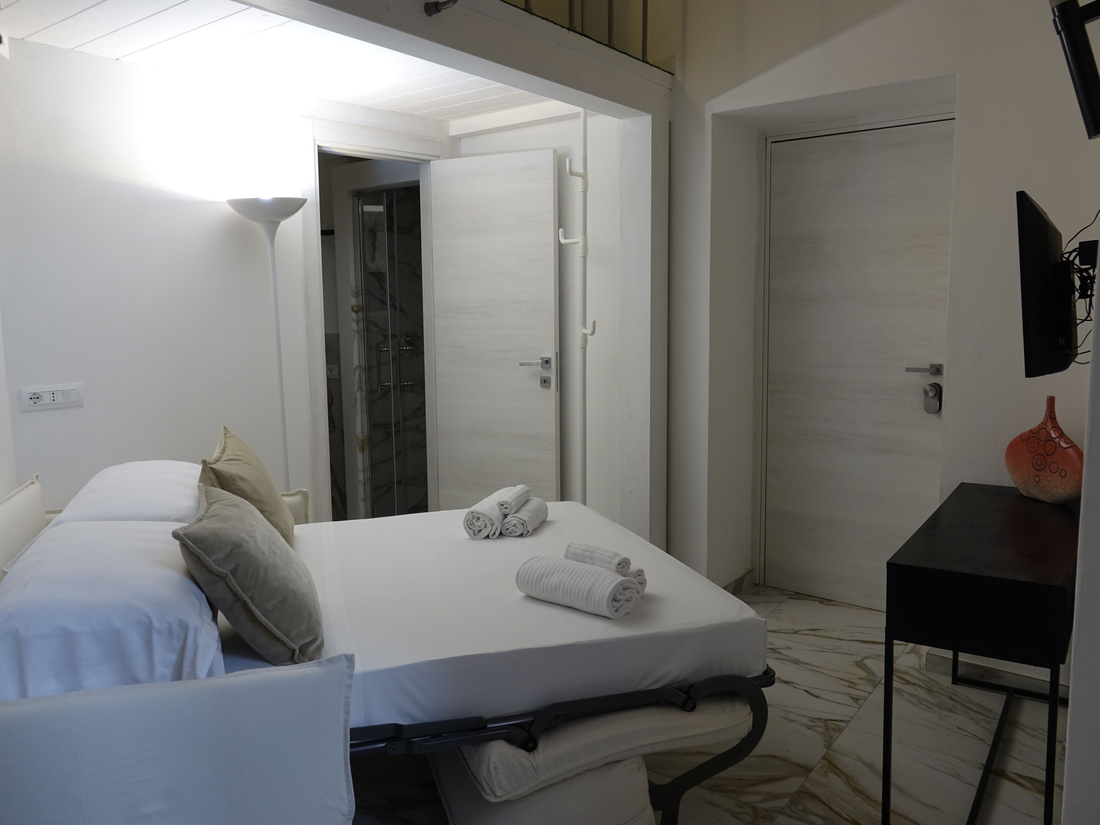 Een hotelkamer met een bed, een bureau, een douche en een deur.