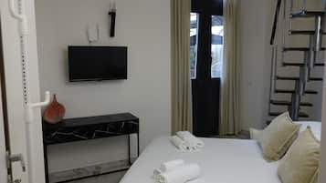 Habitación de hotel con cama, televisor de pantalla plana montado en la pared, una mesita consola con diseño de mármol y una ventana con cortinas.