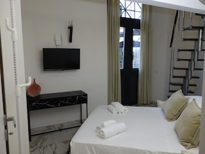 Habitación de hotel con cama, televisor de pantalla plana montado en la pared, una mesita consola con diseño de mármol y una ventana con cortinas.