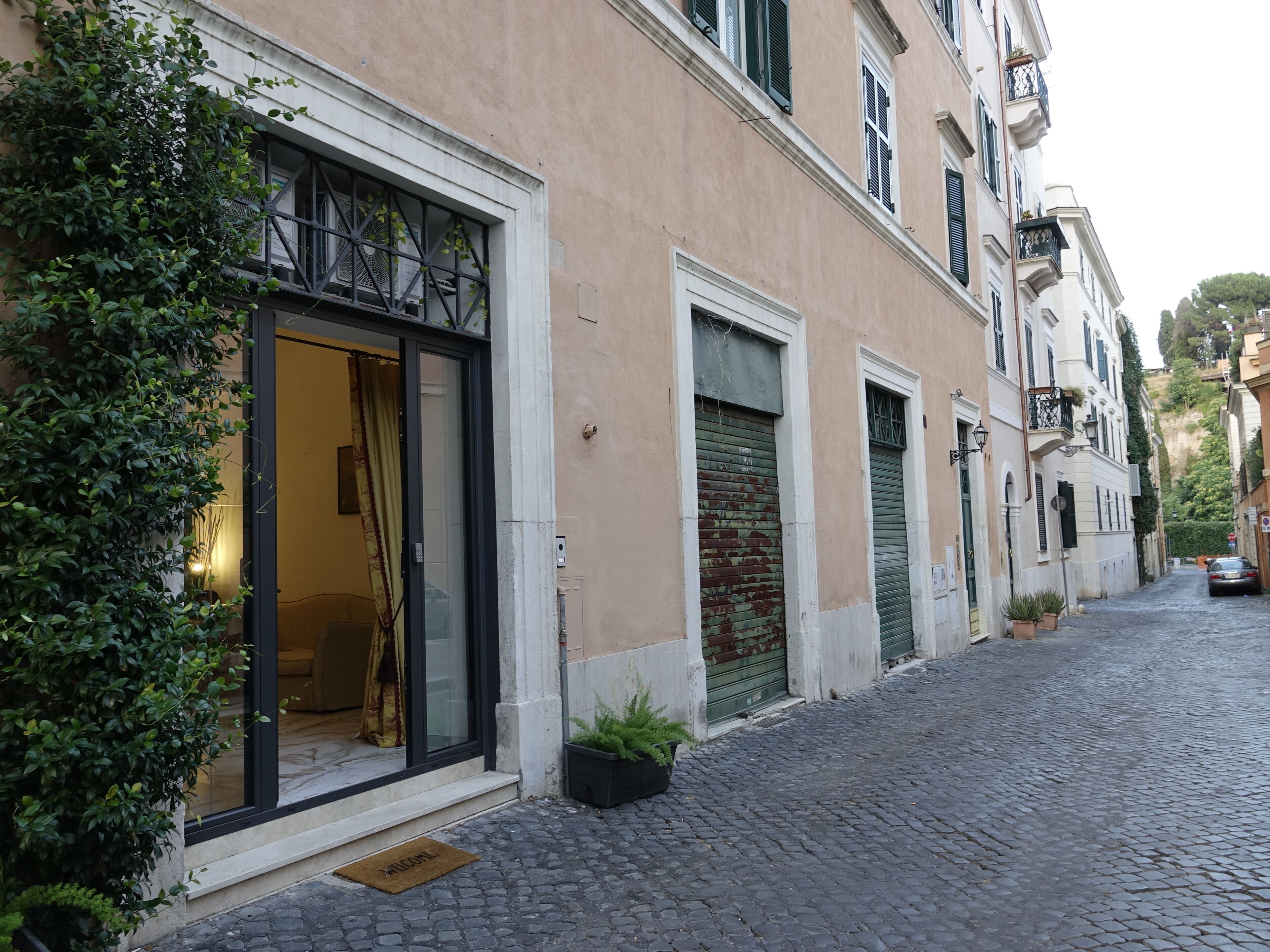 A building with a glass entrance, a closed shutter door, and a cobblestone street.