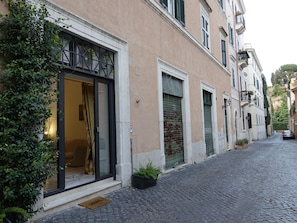 Um edifício com entrada de vidro, uma porta com persiana fechada e rua de paralelepípedos.