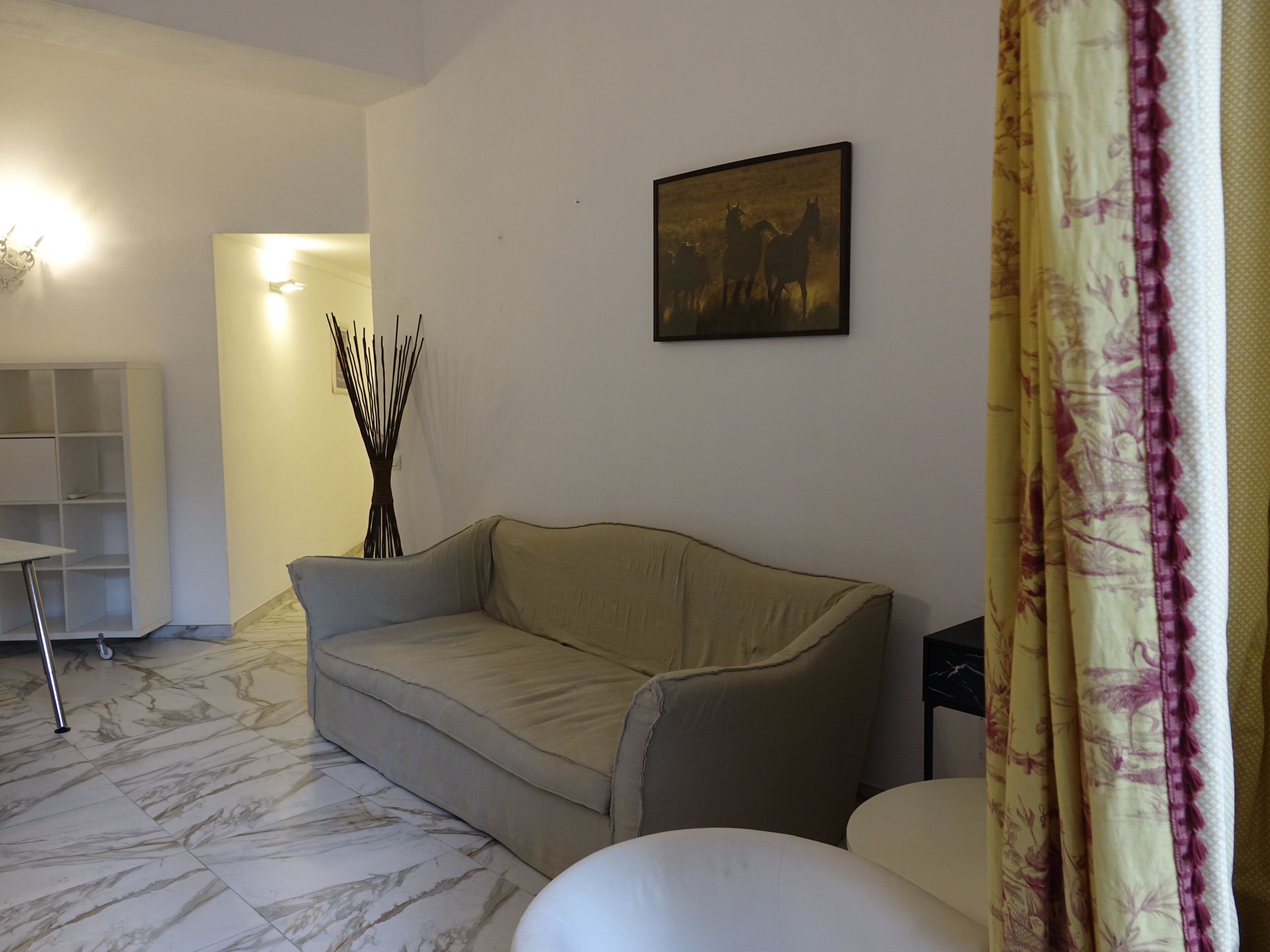 A living room with a sofa, a coffee table, a side table, a lamp, a picture frame, and a curtain.