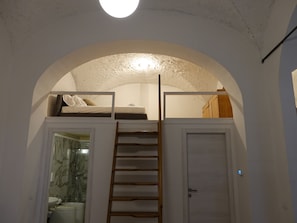 Quarto com beliche, escada de madeira, banheiro com chuveiro de mármore e porta branca.