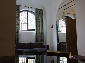 Um quarto com uma janela grande, um sofá, uma cadeira de madeira e um espelho.