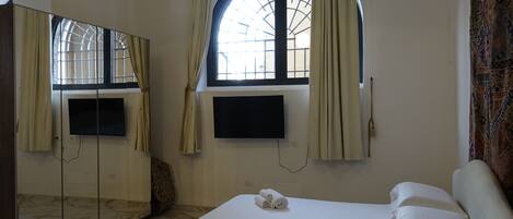 Een hotelkamer met een bed, een aan de muur bevestigde televisie, een grote spiegel en een raam met gordijnen.
