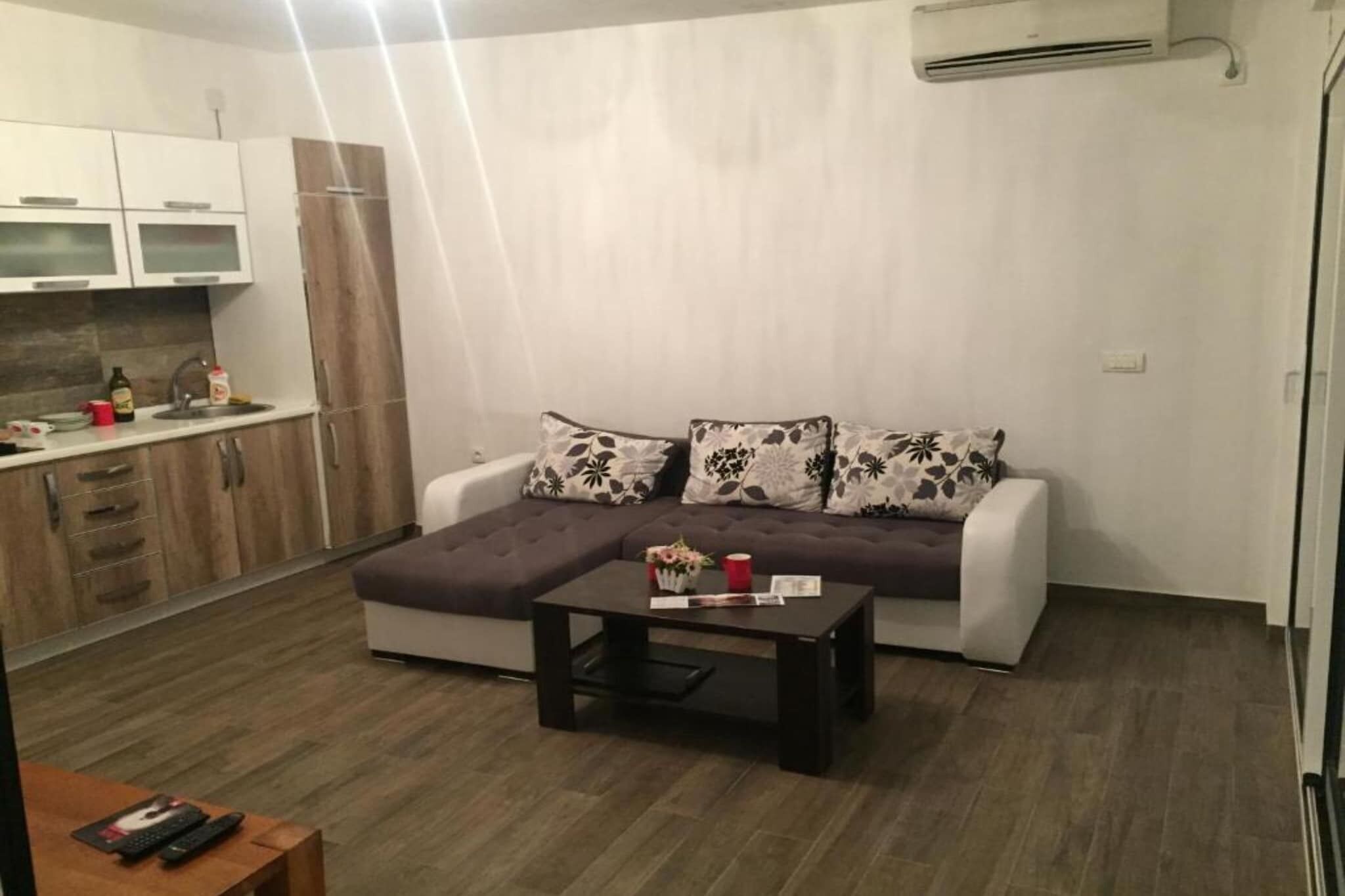 Ein modernes Wohnzimmer mit Ecksofa, Couchtisch und Küchenbereich mit Schränken und Arbeitsplatte.