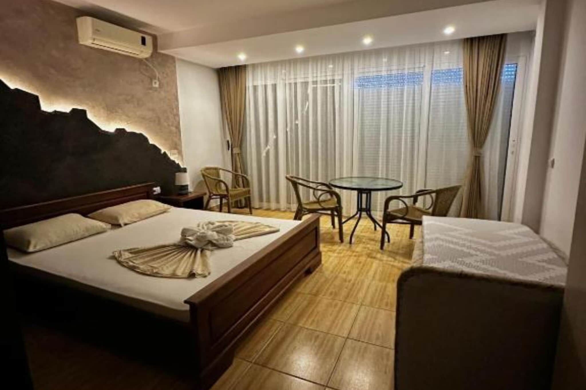 Habitación de hotel con una cama, una mesa redonda, dos sillas, una mesita y una ventana con cortinas.