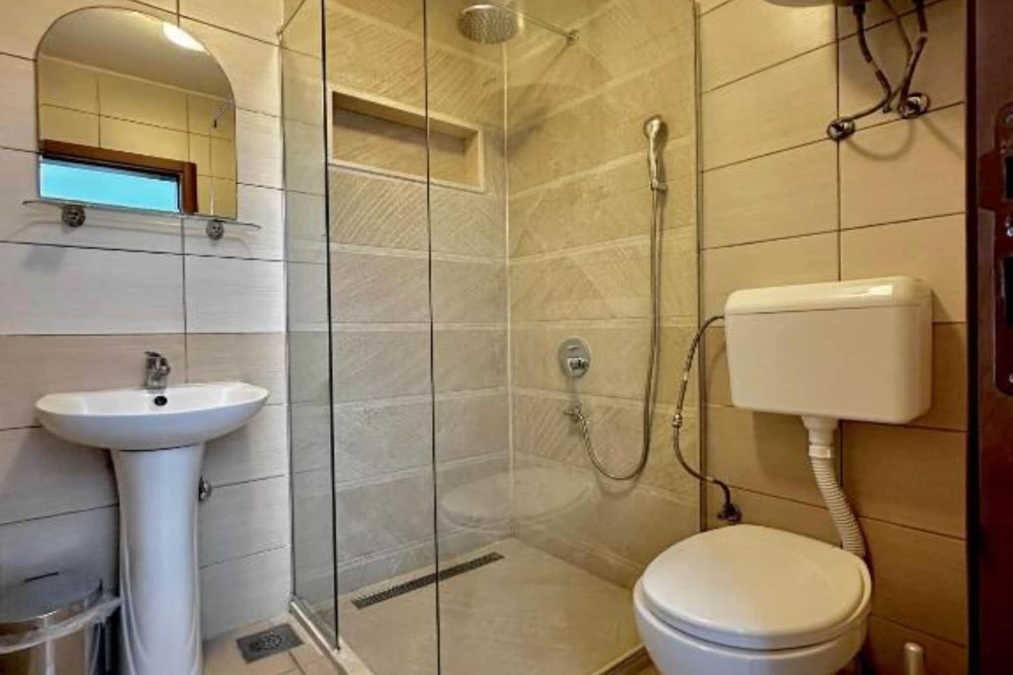 Kylpyhuone, jossa on lasiseinällä varustettu suihku, jalkapallin muotoinen allas ja wc.