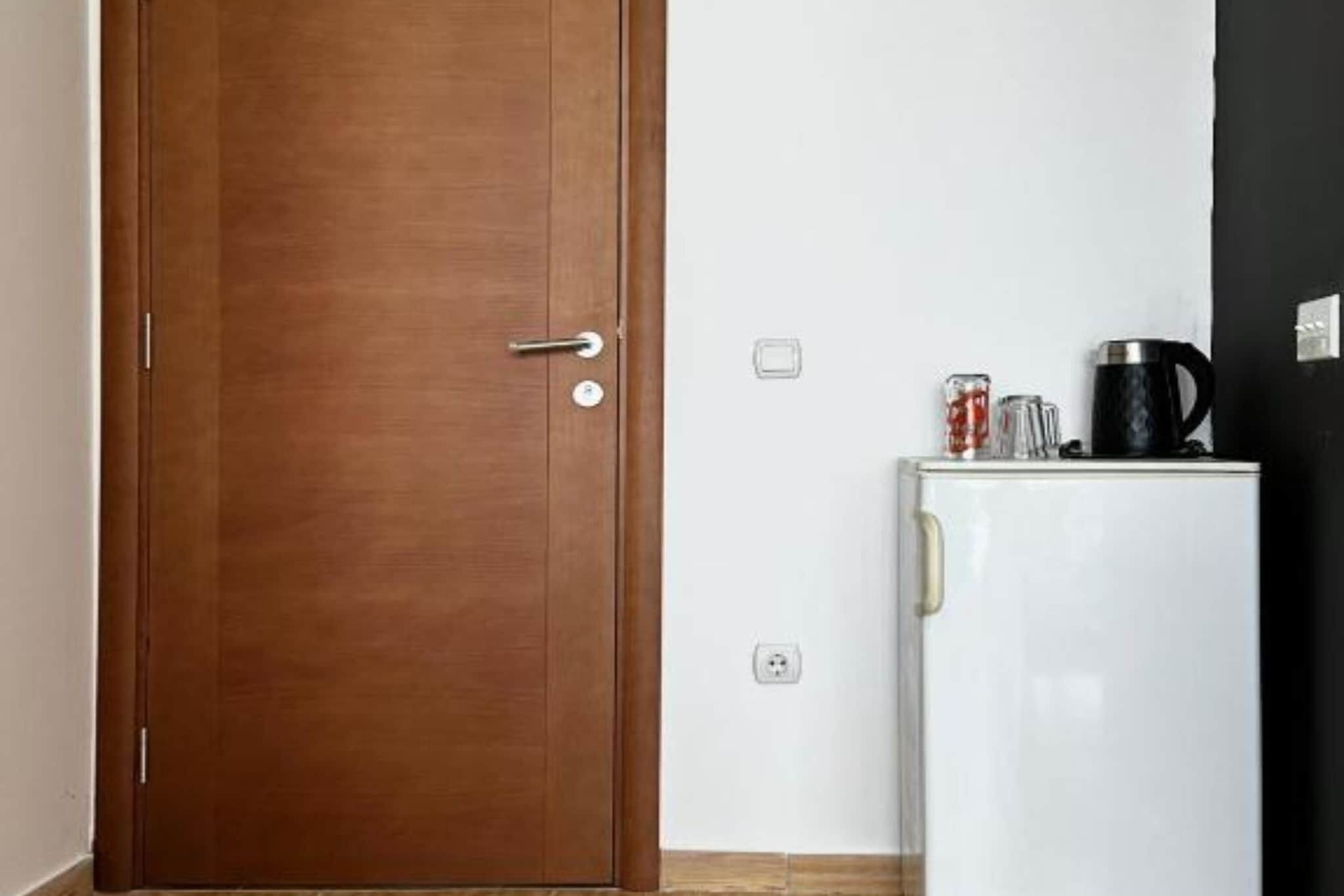Una puerta de madera cerrada con manija y un refrigerador blanco con una cafetera negra y un vaso encima.